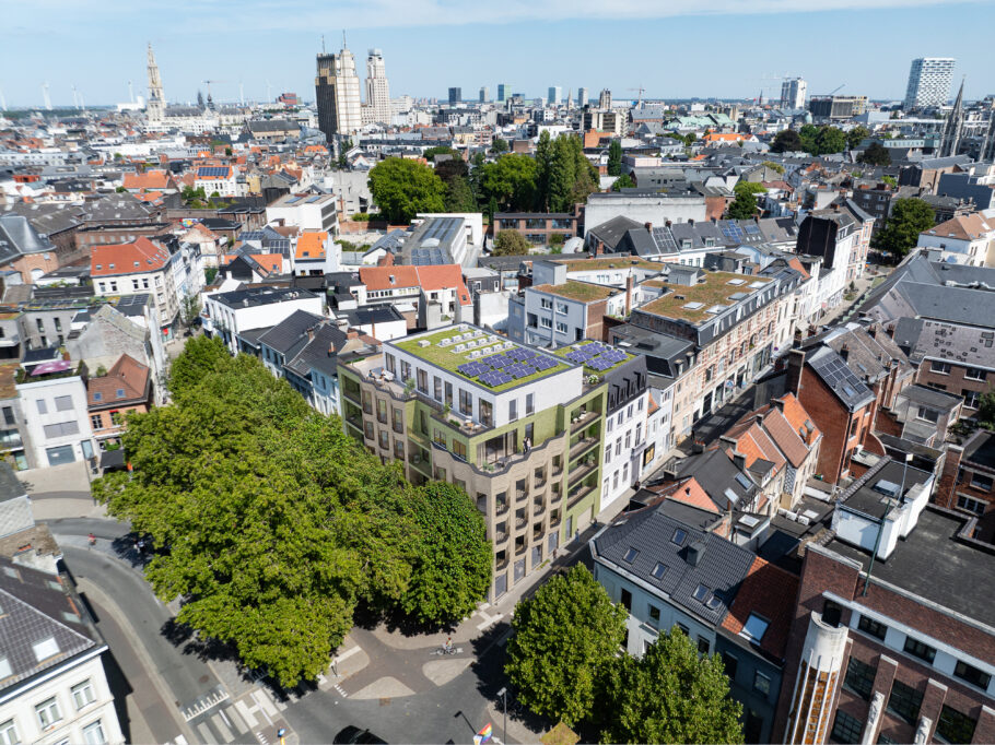 Aerial view with a 3D integration of a corner building with balconies and a planted roof, surrounded by streets, trees and urban buildings.